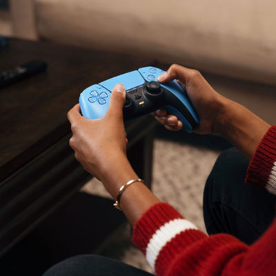 Nahaufnahme einer Person, die mit beiden Händen einen DualSense Wireless-Controller in Starlight Blue hält.