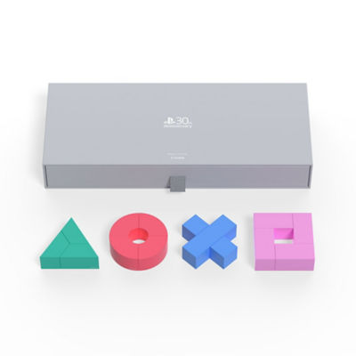 Graue Box zusammen mit den Magnetblöcken in Form eines grünen Dreiecks, roten Kreises, blauen Kreuzes und pinkfarbenen Quadrats.