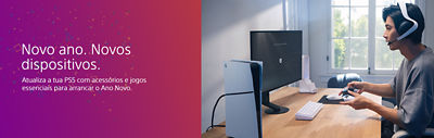 Uma configuração PS5 num quarto iluminado: uma consola PS5 está sobre uma secretária de madeira ao lado de um monitor, um teclado branco e acessórios. À direita, uma pessoa com headset segura um comando DualSense. À esquerda, o fundo colorido com confettis apresenta o texto “Novo ano. Novos dispositivos.” e “Atualiza a tua PS5 com acessórios e jogos essenciais para arrancar o Ano Novo.”
