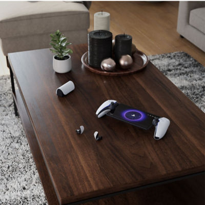 PlayStation Portal Remote-Player auf einem Holztisch zusammen mit PULSE Explore Wireless-Ohrhörern und Lade-Case