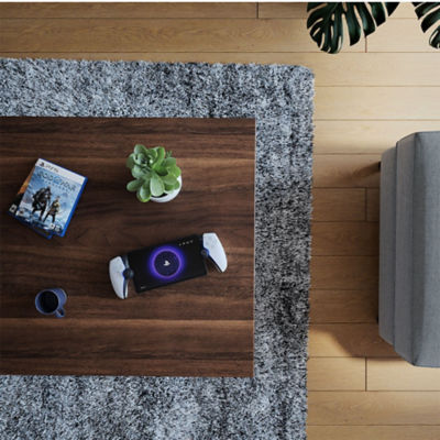 PlayStation Portal Remote-Player auf einem Holztisch zusammen mit einer Pflanze und dem PS5-Spiel God of War Ragnarök in seiner Verpackung