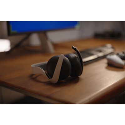 Un casque PULSE Elite blanc posé sur un bureau, tourné vers le haut, devant l'écran et le clavier d'un PC