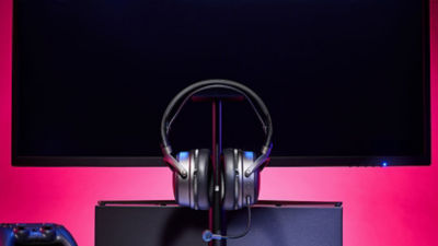 Audeze Maxwell 2 headset displayed on a stand in front of a monitor with pink lighting.