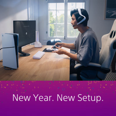 A PS5 gaming setup in a bright room: A PS5 console is placed on a wooden desk next to a monitor, a white keyboard, and accessories. On the right, a person wearing a headset sits in a gaming chair holding a DualSense controller. Below the image, a purple banner with confetti displays the text “New Year. New Setup.”