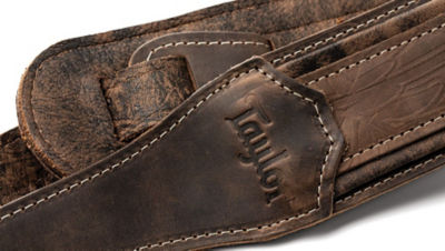 Close up of brown leather guitar strap with logo and pattern details 