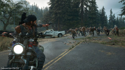Days Gone star Deacon St. John riding a motorcycle to escape a horde of zombies while pointing a gun at them.